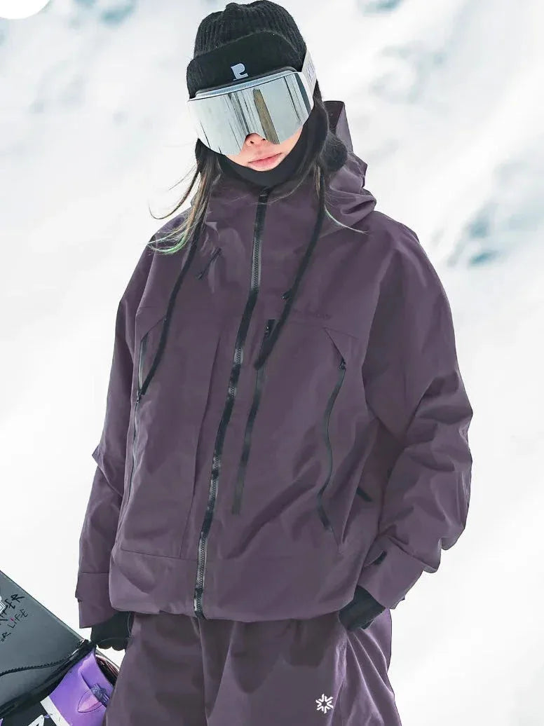 Woman in mauve-purple hooded ski jacket with black zip pockets and drawstring hood on the snowy mountainside