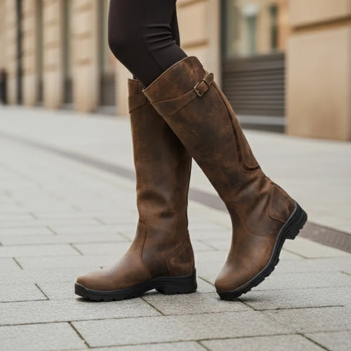Close-up of brown leather knee high boots with buckle fastening, worn with black trousers on a city pavement