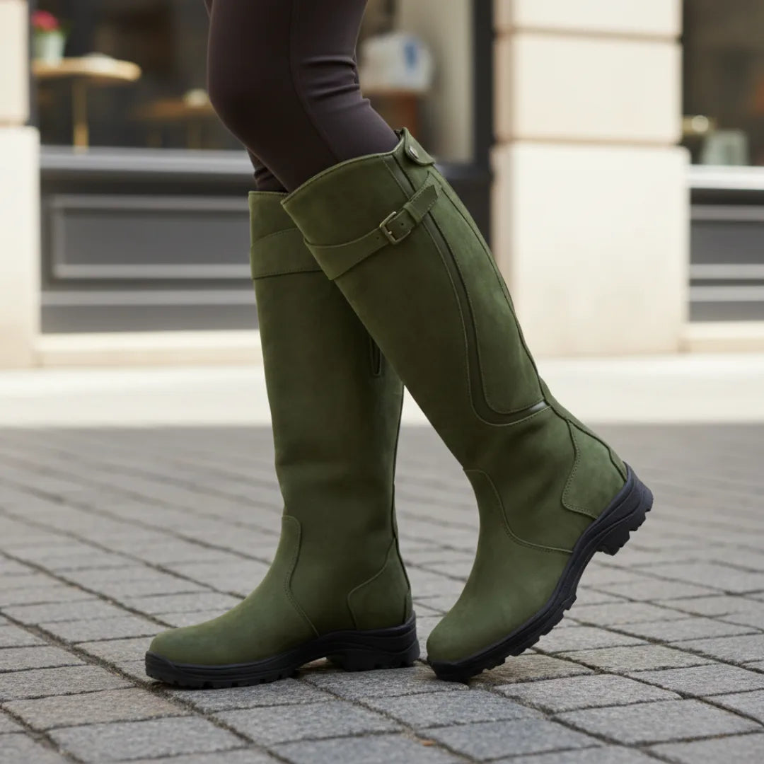 Green suede-finish knee high boots with buckle strap, side profile on a paved city street
