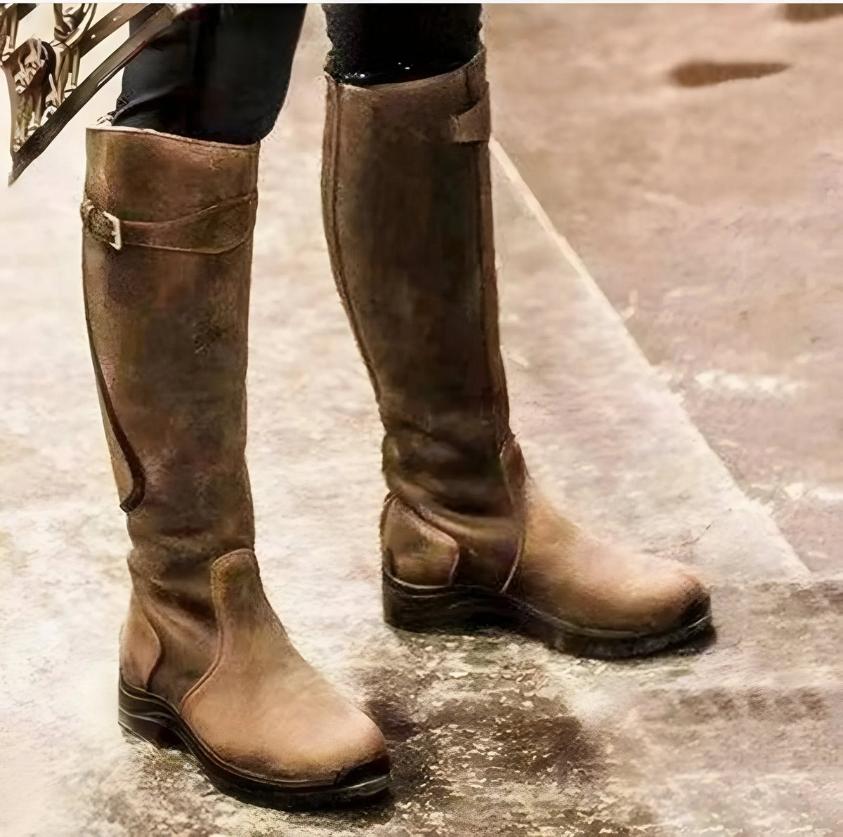 Distressed tan leather knee-high boots with buckle straps, front view on a paved surface