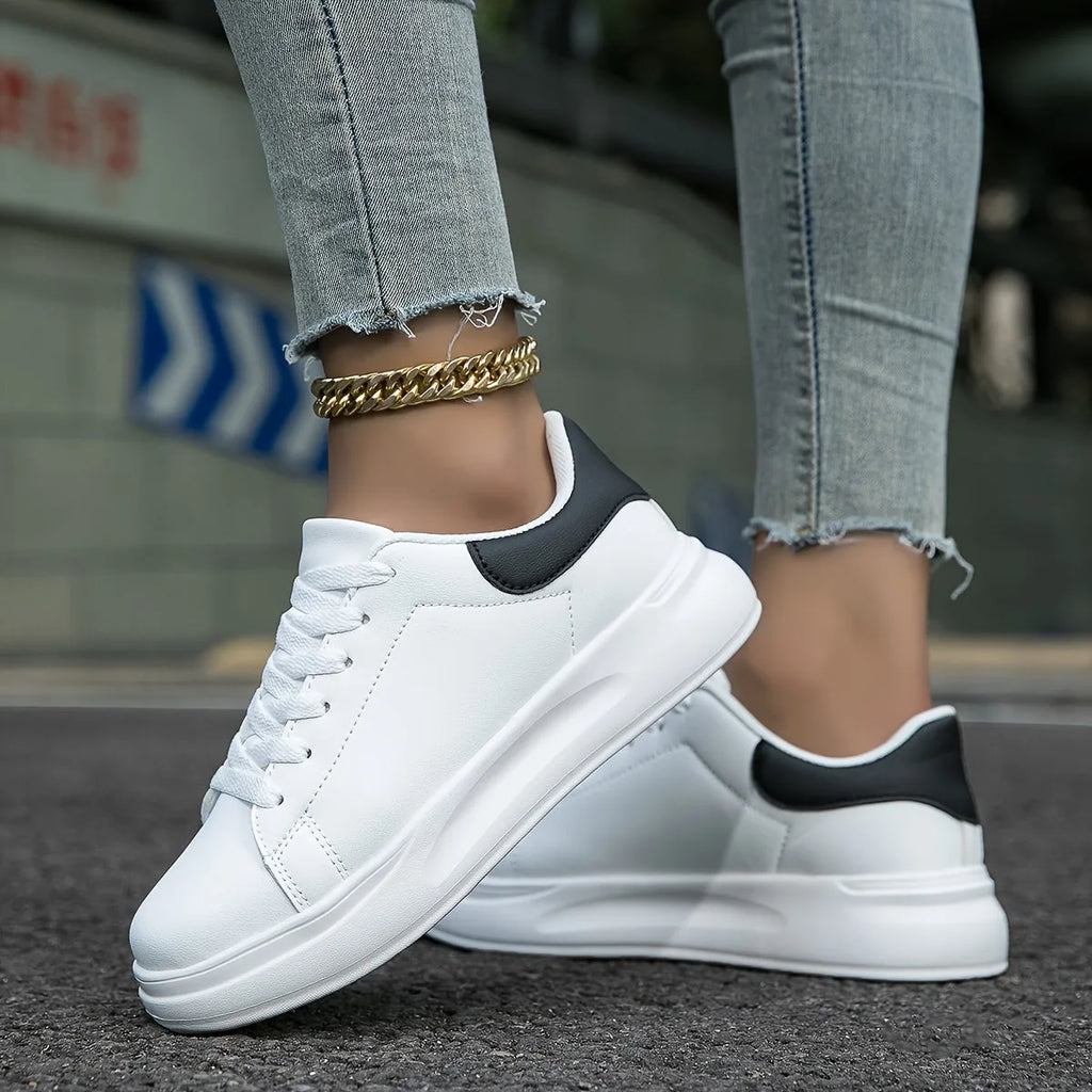 Angled view of both white trainers with black accents, laces tied, on asphalt ground