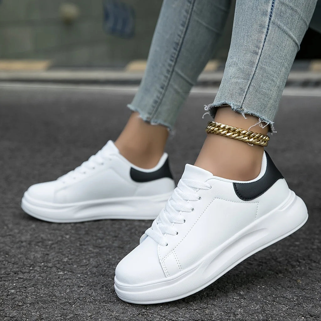 Front-facing close-up of white lace-up trainer with black heel detail while walking