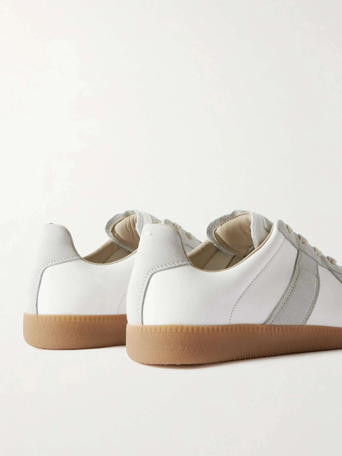 Close-up rear view of two white leather trainers showing the suede heel tab and tonal stitching
