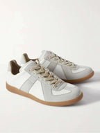 Front three-quarter view of a paired white leather and suede trainer with cream laces and gum sole