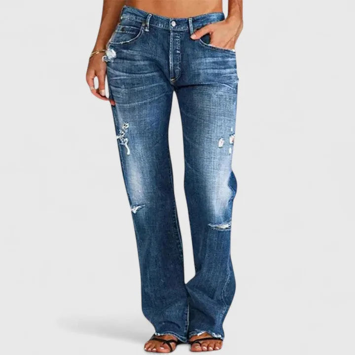 Close-up front view of mid-blue distressed jeans showing frayed rips at the thigh and knee.