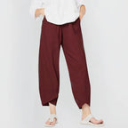 Front view of deep burgundy wide-leg linen-blend trousers with wrap-style curved hem, paired with sandals