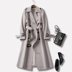 Light grey trench coat with buckled belt and storm flap, styled flat lay with a quilted handbag and black heels
