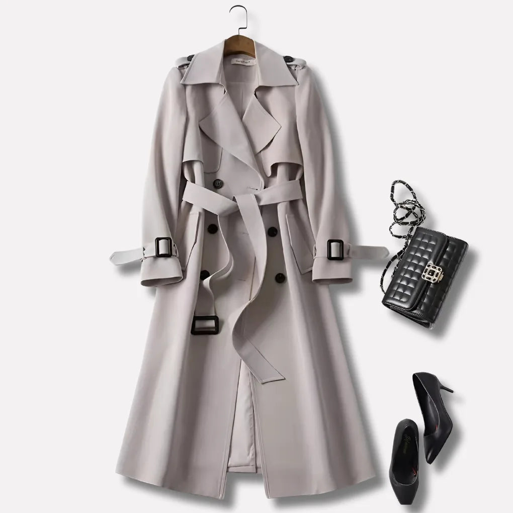 Light grey trench coat with buckled belt and storm flap, styled flat lay with a quilted handbag and black heels