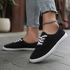 Black canvas lace-up trainers with white laces and white soles, shown from the side while walking on grey paving.