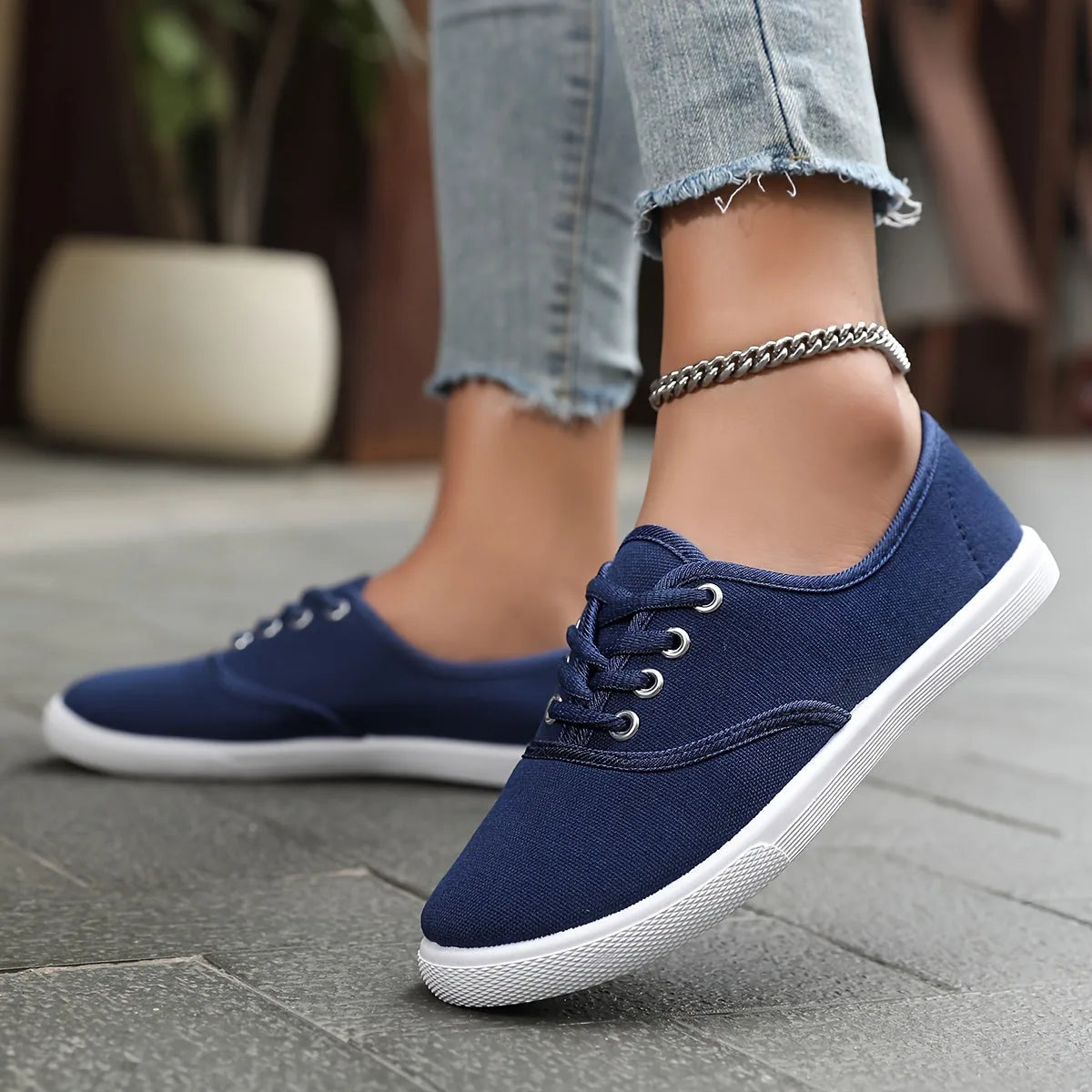 Navy blue canvas lace-up trainers with white soles, paired with cropped denim jeans and a silver anklet.