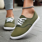 Khaki green canvas lace-up trainers with white laces and soles, close-up side angle on a stone pathway.