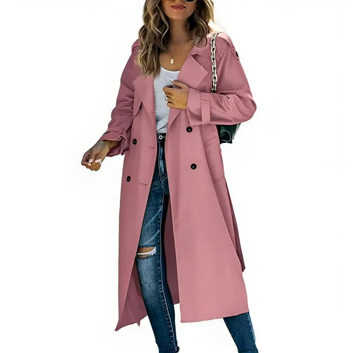 Woman wearing a dusty pink double-breasted trench coat with belted cuffs, open over jeans and a white top.