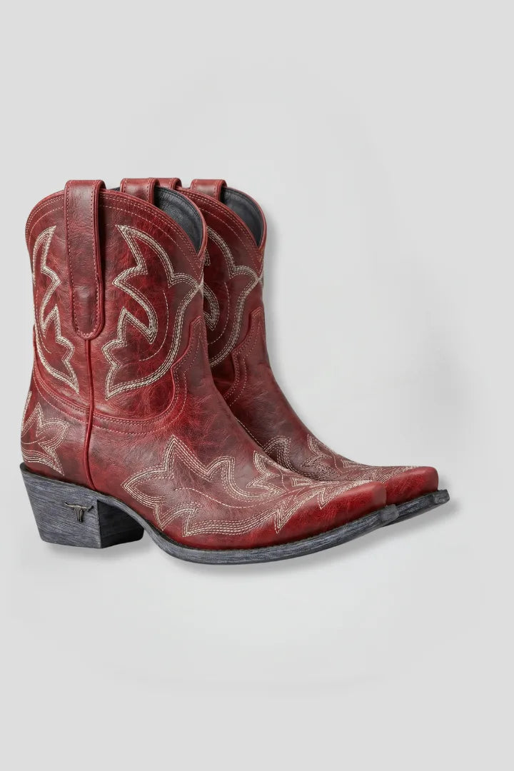 Side view of red leather cowboy boots with cream Western embroidery, pointed toe and stacked heel with metal longhorn detail