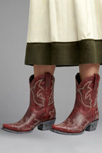 Front angle of red leather Western boots with pointed toe worn beneath a flowing midi skirt