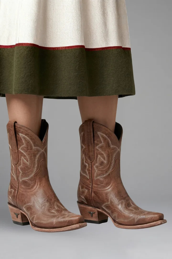Front view of brown leather cowboy boots with embroidered stitching worn under a layered skirt hem