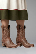 Front view of brown leather cowboy boots with embroidered stitching worn under a layered skirt hem