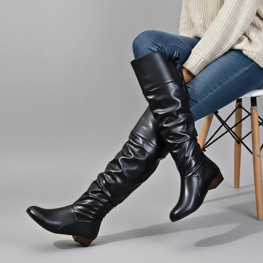 Black over-the-knee slouch boots with ruched leather shaft, worn with jeans and a cream jumper.