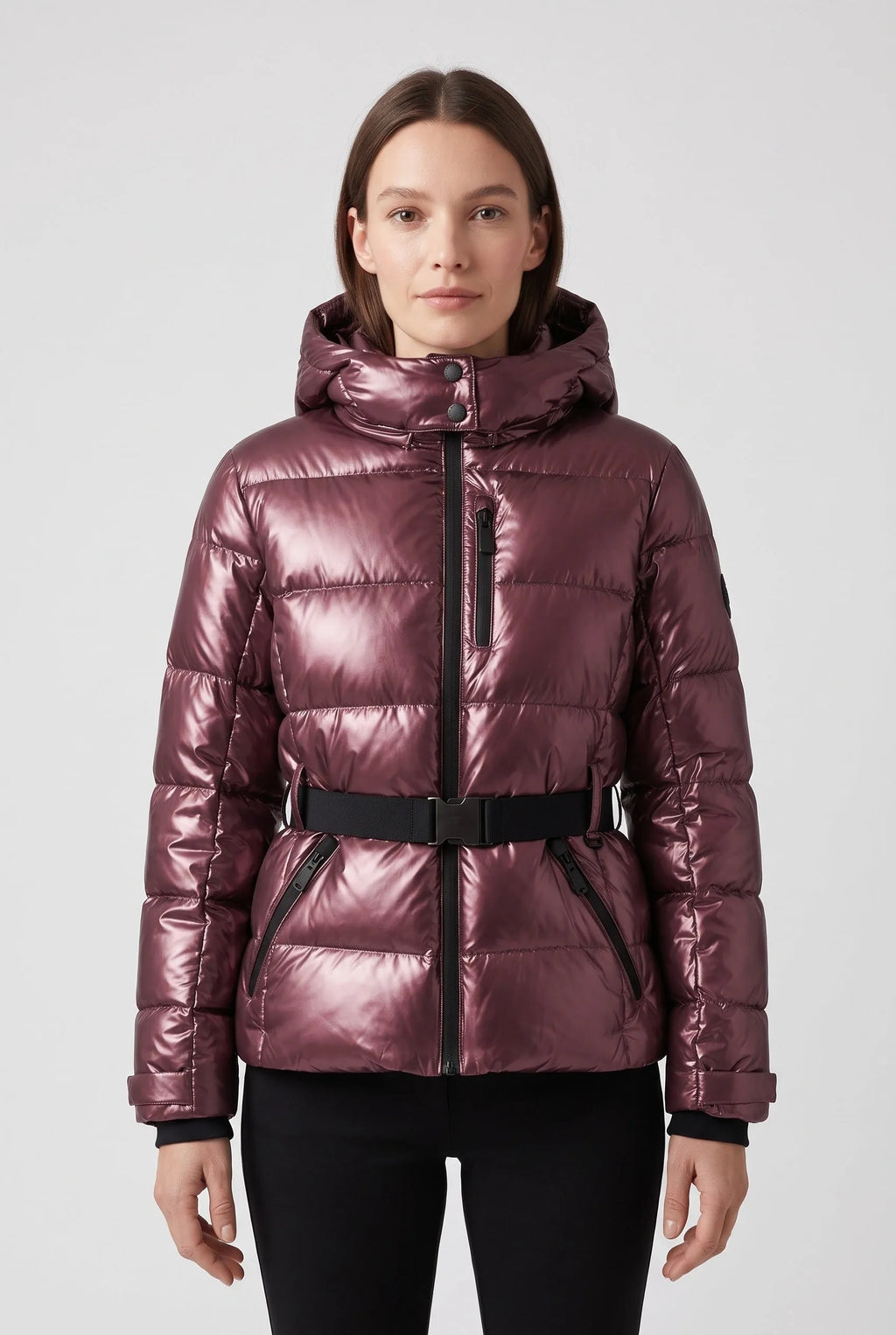 Front view of a woman wearing a metallic burgundy hooded puffer jacket with belted waist and black zip