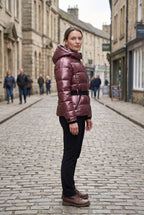 Woman wearing the metallic burgundy puffer jacket on a cobbled street, styled with black trousers and boots