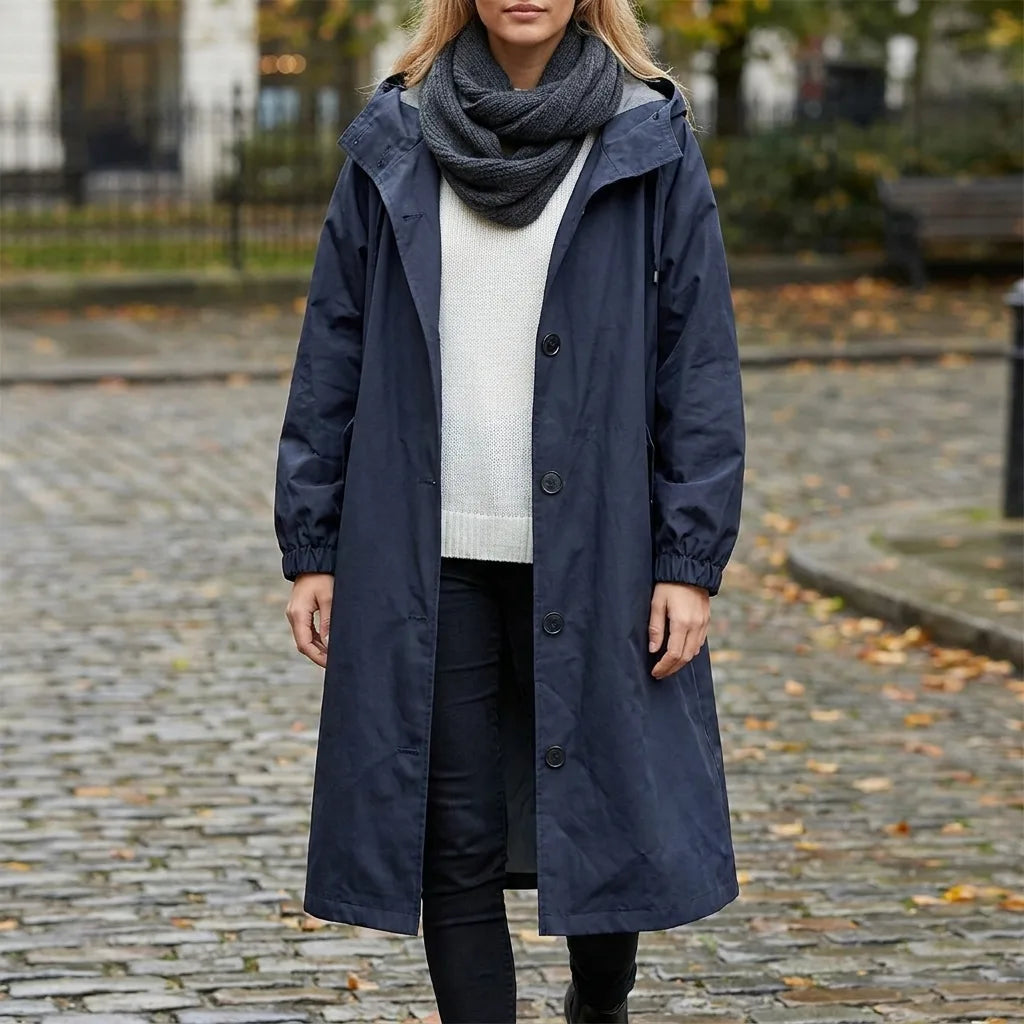 Navy hooded raincoat worn outdoors on a cobbled street, full length front view showing long hem and relaxed silhouette