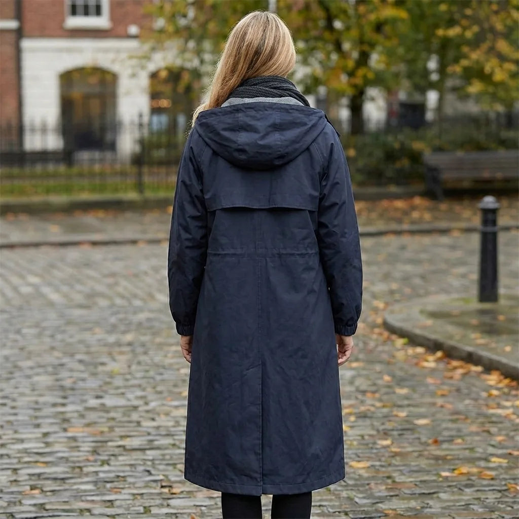 Back view of the navy hooded raincoat outdoors, showing the hood, yoke seam and straight below-knee hem