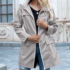 Grey hooded zip-up trench coat with contrast trim, worn open over a black top and blue jeans