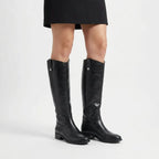 Front view of a woman wearing knee-high black leather boots under a black dress, shown with both legs together