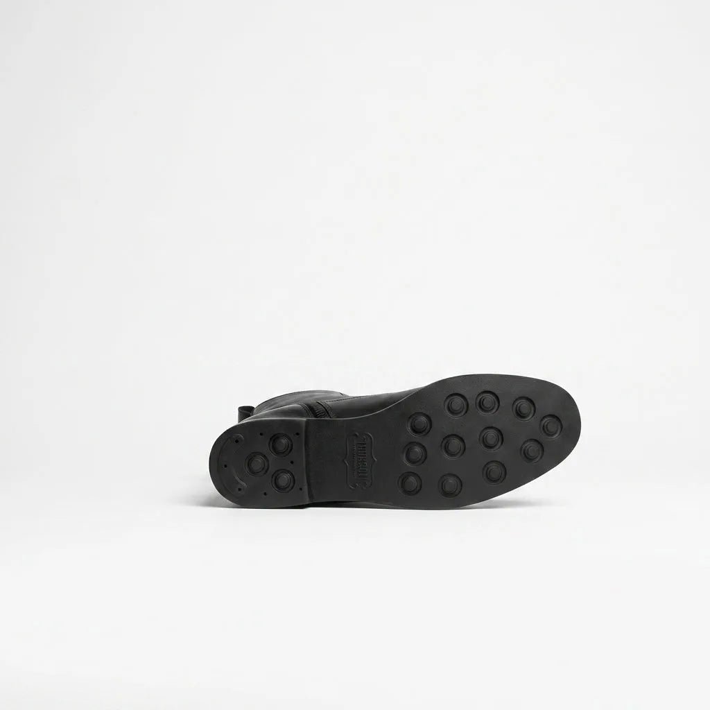 Close-up of the ridged rubber sole of a black leather knee-high boot, showing the grip pattern and branding
