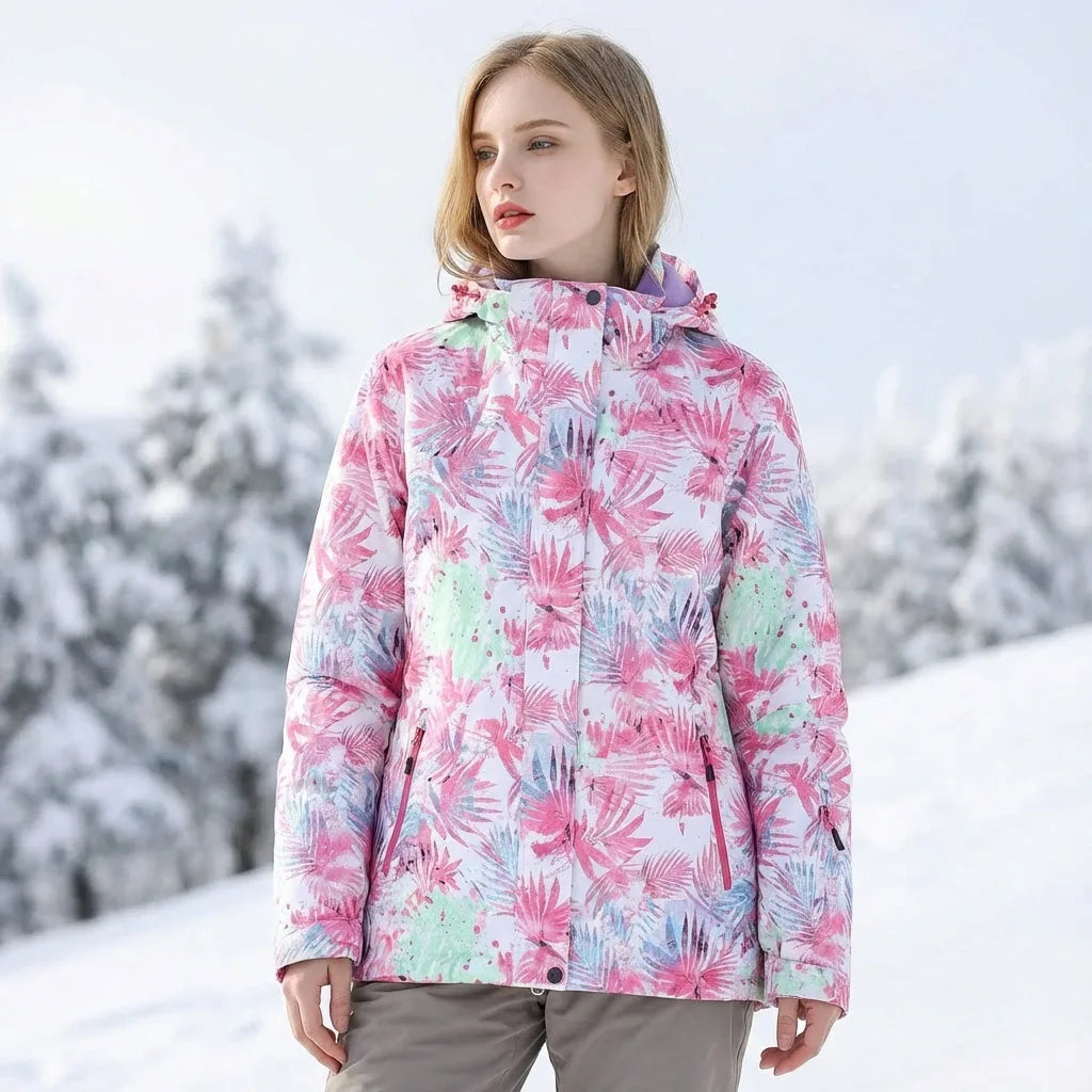 Woman on a snowy slope wearing a pink floral print hooded ski jacket with zip pockets and drawstring hem