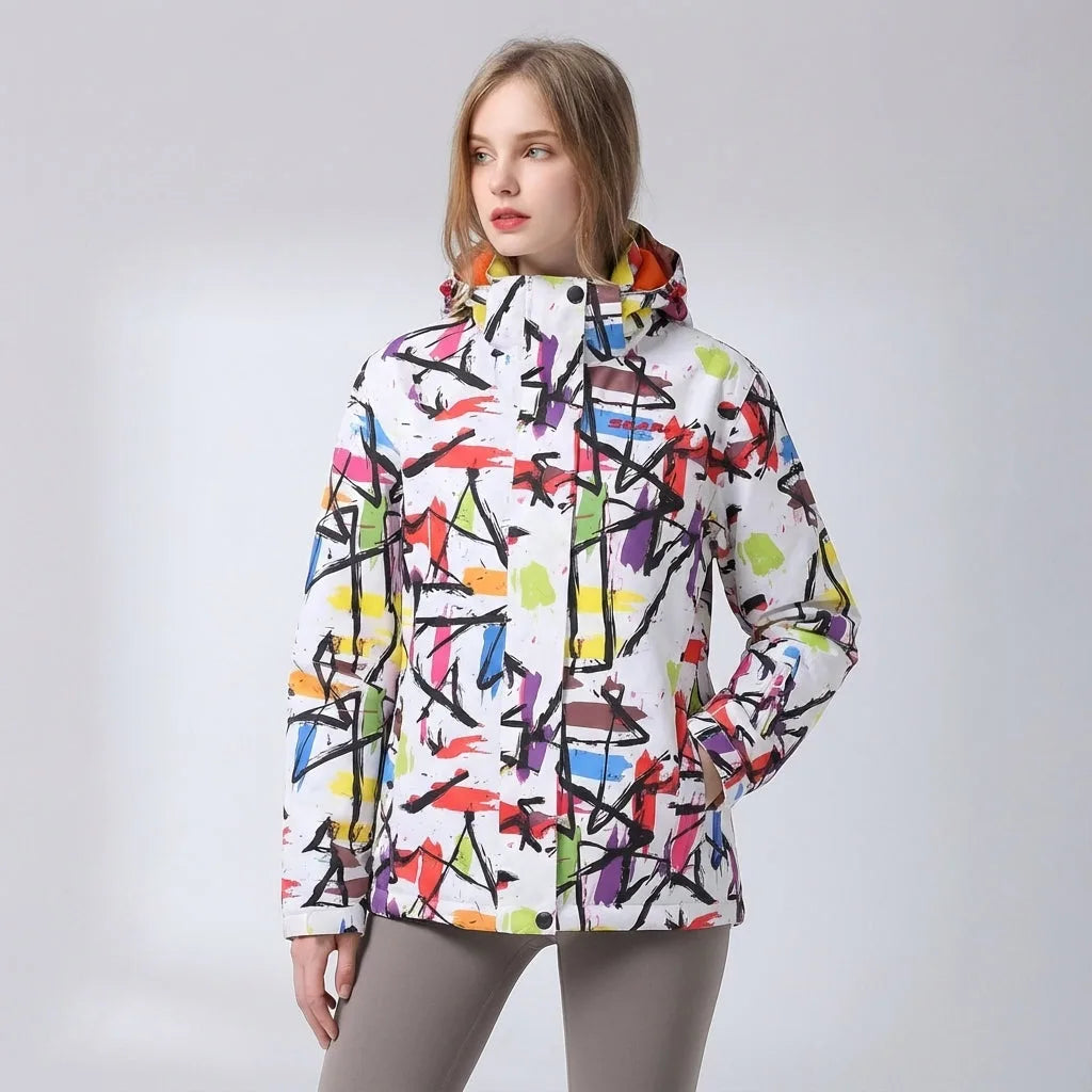 Front-facing shot of the pink floral hooded jacket paired with grey trousers against a snowy backdrop