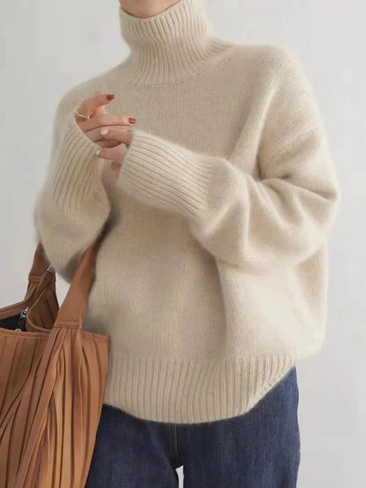 Close-up front view of a cream polo neck jumper with ribbed collar and sleeves, worn with a tan pleated tote bag