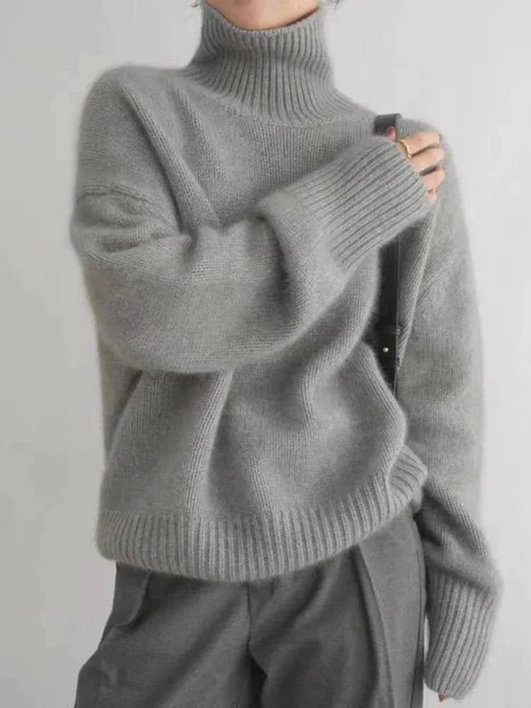 Grey polo neck jumper with ribbed knit texture, worn with a black crossbody bag and grey trousers