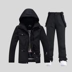 Black two-piece ski set with hooded jacket and bib-style trousers, worn with white trainers