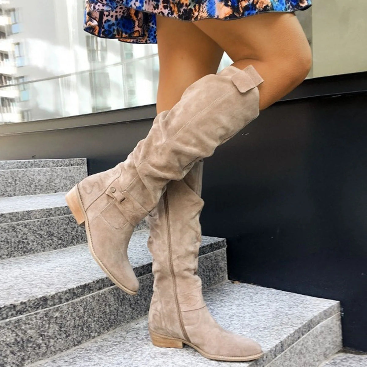 Close-up side profile of beige suede knee-high boots showing slouch folds and side zip