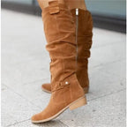 Tan suede knee-high slouch boots with buckle detail photographed against a stone pavement