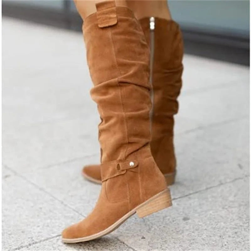 Tan suede knee-high slouch boots with buckle detail photographed against a stone pavement
