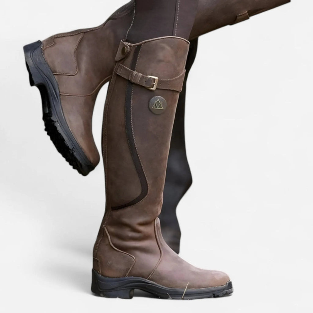 Side view of knee-high brown leather boot with buckle strap detail, worn with knee raised showing textured sole