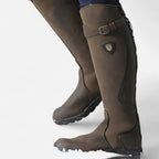 Close-up rear view of two brown leather knee-high boots with buckle strap and shield-shaped logo patch