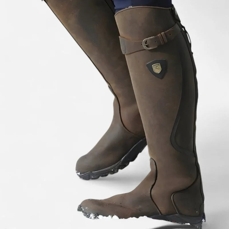 Close-up rear view of two brown leather knee-high boots with buckle strap and shield-shaped logo patch
