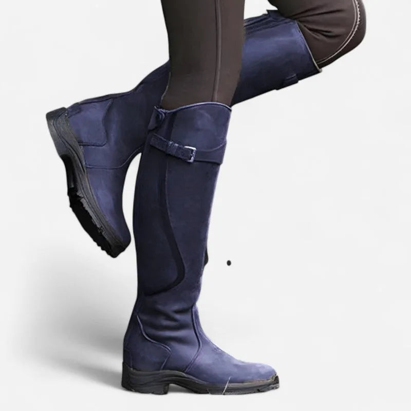 Navy blue suede-look knee-high boots with buckle strap, side profile with one leg raised to show the sole