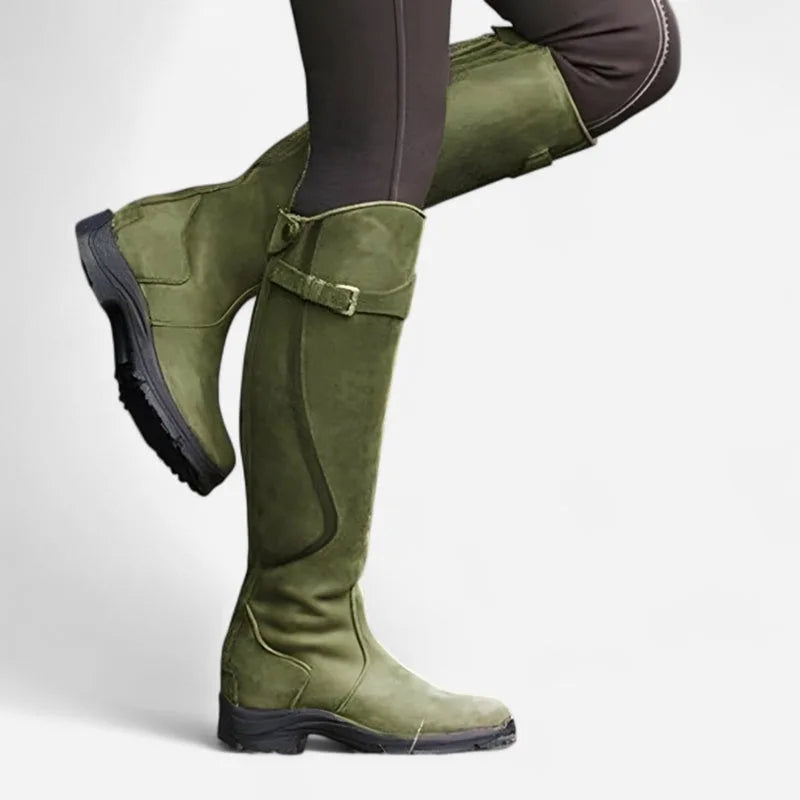 Olive green knee-high leather boots with buckle strap detail, side view with leg lifted to display the tread