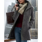 Grey textured wool coat with turndown collar worn open over a burgundy jumper in a snowy city setting