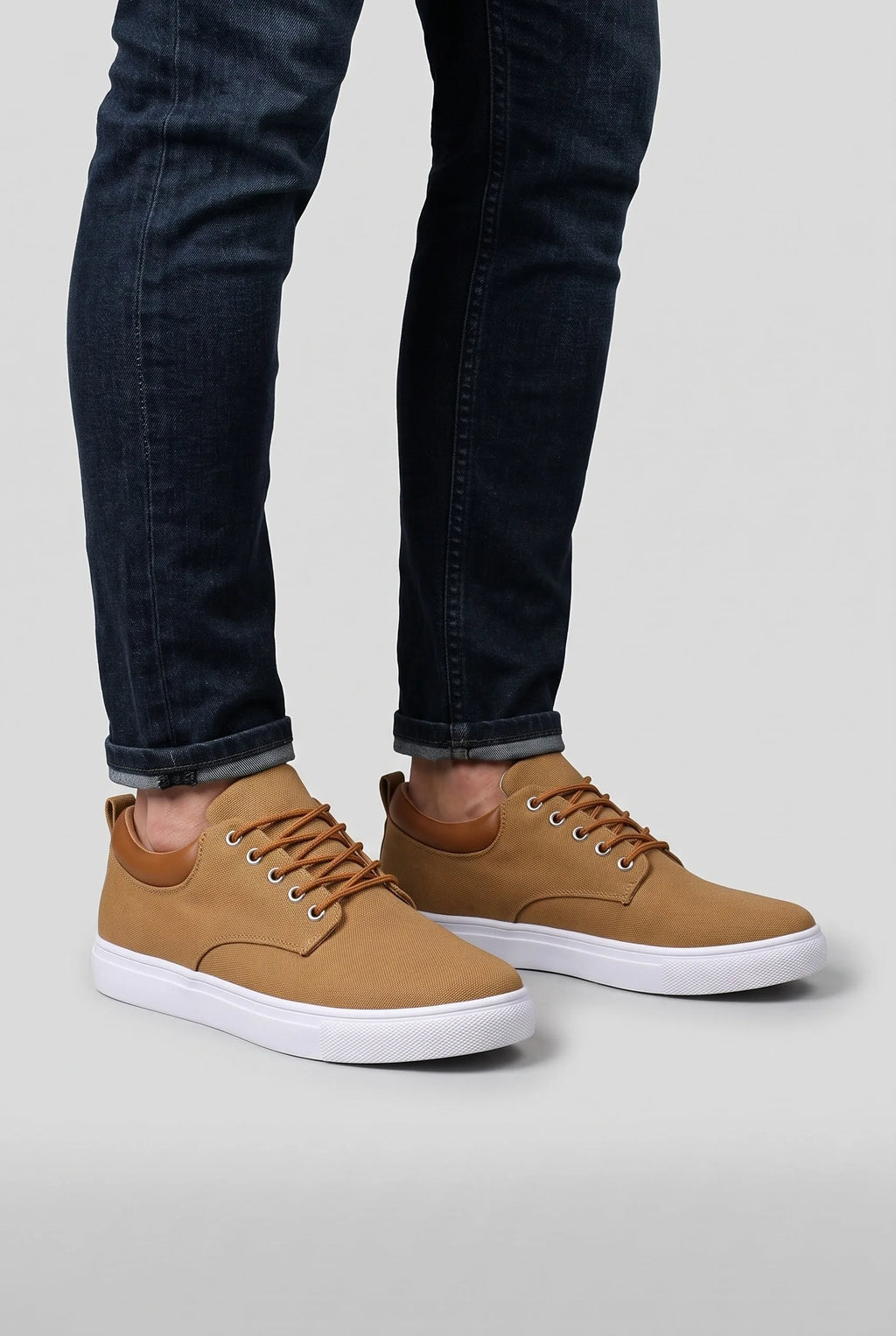 Tan woven trainers worn with rolled dark denim jeans, shown from the ankle down