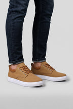 Tan woven trainers worn with rolled dark denim jeans, shown from the ankle down